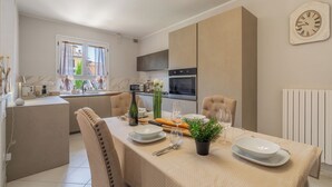 A modern kitchen with a dining area set for a meal, featuring a clock, a stove, and a window with a view. - Casa Vellaria – Charming Home with Garden in Tuscany near Pisa & Florence (Forcoli)