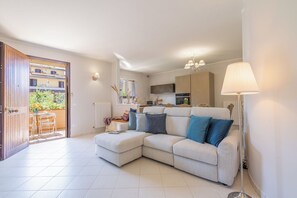 Ein Wohnzimmer mit einer Couch, einem Esstisch und Stühlen, einer Küchenzeile und Blick durch eine geöffnete Tür.