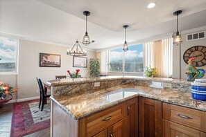 Una cocina con encimeras de granito, armarios de madera, iluminación colgante y un amplio ventanal con vistas.