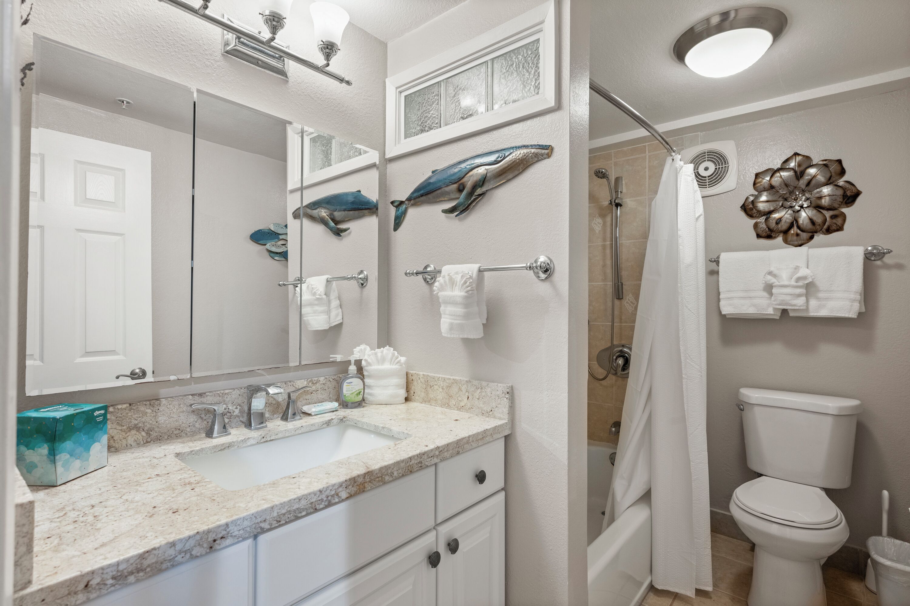Un baño con lavamanos, espejo, toallero, ducha, inodoro y detalles decorativos en la pared.