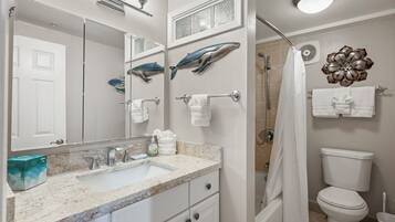 Un baño con lavamanos, espejo, toallero, ducha, inodoro y detalles decorativos en la pared.