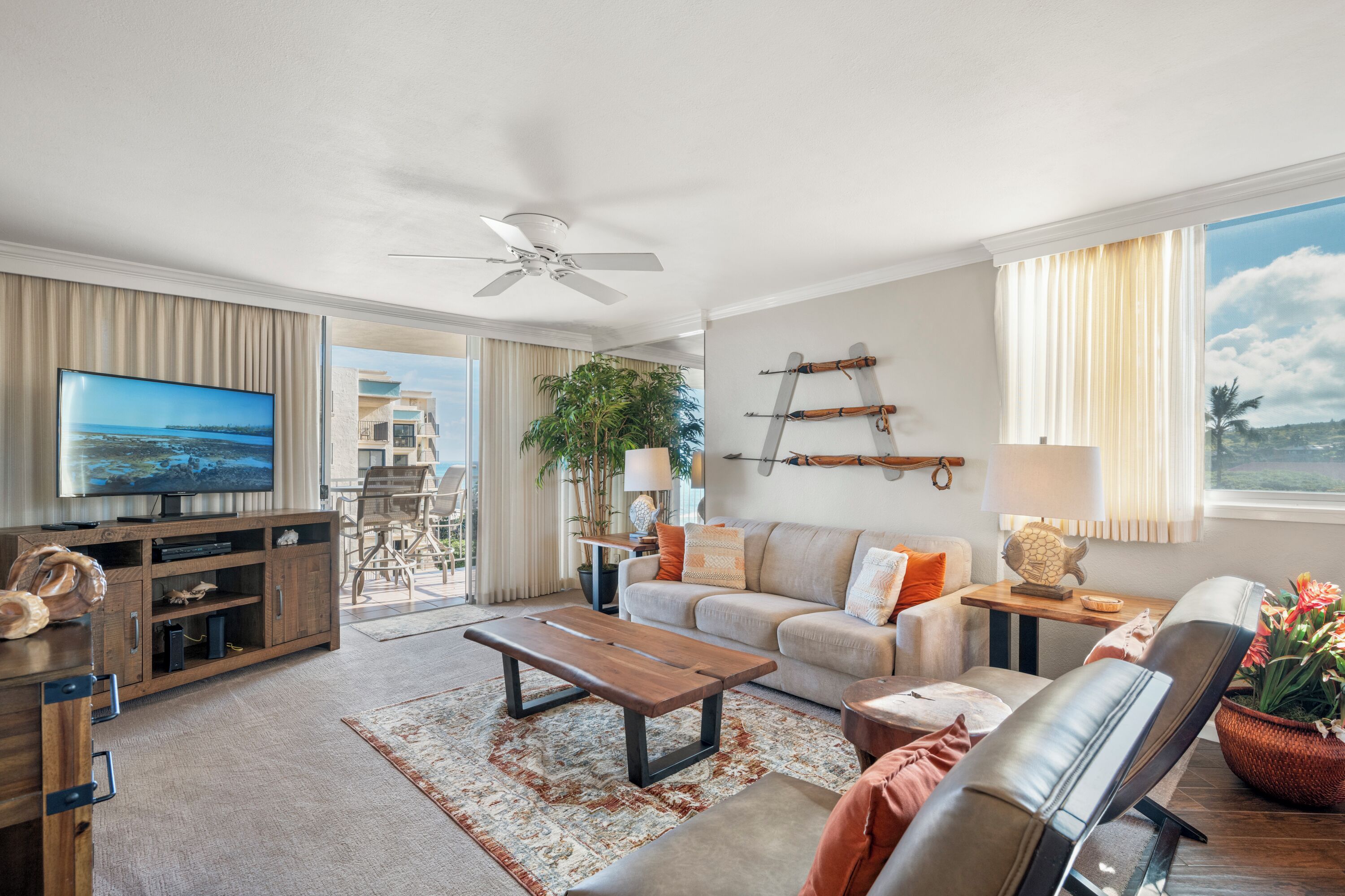 A spacious living room with a flat-screen TV, a ceiling fan, a sofa, a coffee table, and a view of the outdoors.