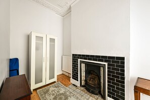 A room with a fireplace, a wardrobe, and a blue bag. - GuestReady - Stylish 1bed w Backyard in Clapham (London)