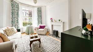 A living room with a fireplace, a sofa, a small table, and a television. - GuestReady - Stylish 1bed w Backyard in Clapham (London)