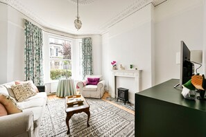 A living room with a fireplace, a sofa, a small table, and a television. - GuestReady - Stylish 1bed w Backyard in Clapham (London)
