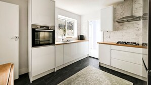 A modern kitchen with white cabinetry, a built-in oven, a gas stove, and a window providing natural light. - GuestReady - Stylish 1bed w Backyard in Clapham (London)