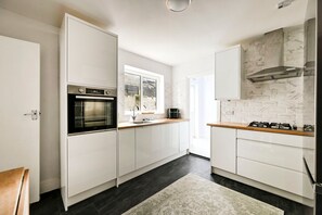 A modern kitchen with white cabinetry, a built-in oven, a gas stove, and a window providing natural light. - GuestReady - Stylish 1bed w Backyard in Clapham (London)