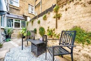 An outdoor seating area with two chairs and a table, surrounded by potted plants and a textured wall. - GuestReady - Stylish 1bed w Backyard in Clapham (London)