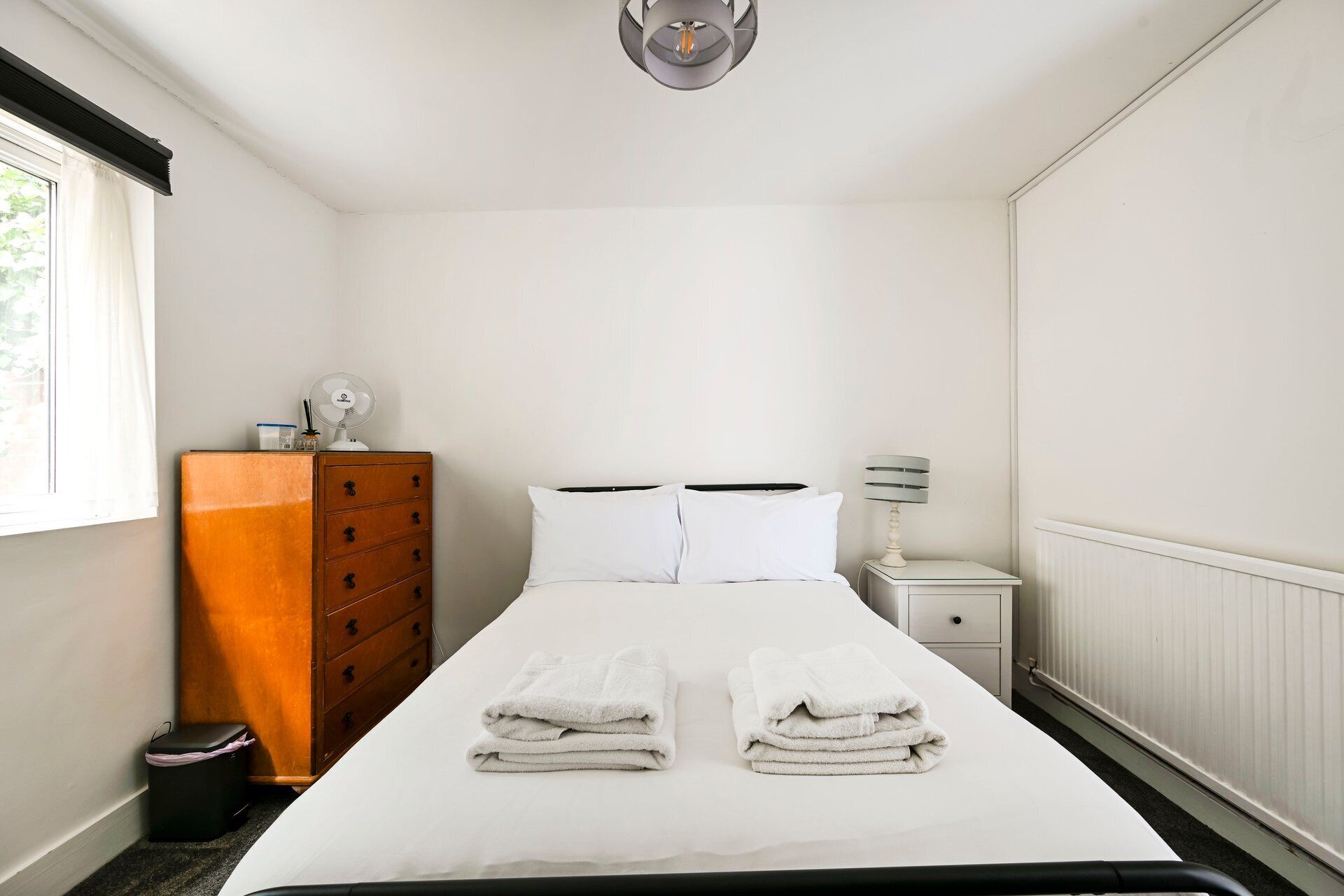 Una habitación de hotel con cama, cómoda, mesita de noche, lámpara y radiador.