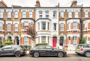 A row of terraced houses with bay windows and a red door. - GuestReady - Stylish 1bed in Clapham with backyard (London)