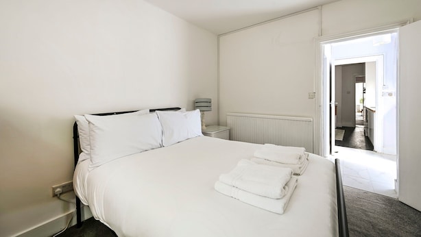 A hotel room with a bed, a nightstand, a lamp, and a view of the outside. - GuestReady - Stylish 1bed w Backyard in Clapham (London)
