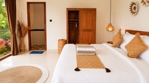 Ein Schlafzimmer mit Bett, Kissen, einem Holzschrank, einer Pendelleuchte und Blick ins Freie.