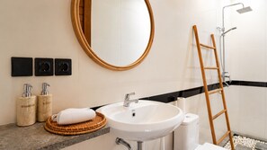 Ein Badezimmer mit einem weißen Waschbecken, einer Holzleiter, einem runden Spiegel und zwei Seifenspendern.