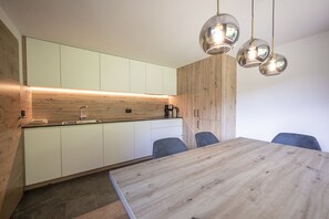Uma cozinha moderna com bancada de madeira, pia e máquina de café. Há uma mesa de jantar com cadeiras.