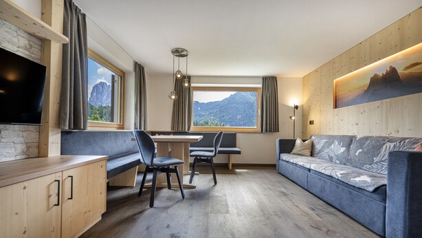 A modern interior with a dining area, seating, and a large window offering a mountain view. - 1015A Valdussa Panoramic Apartment (Ortisei)