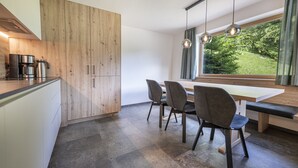 A modern kitchen with a wooden cabinet, a coffee maker, and a dining table with chairs. - 1015A Valdussa Panoramic Apartment (Ortisei)