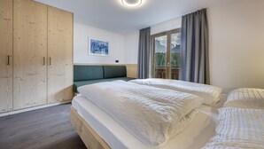 A bedroom with two beds, a wooden wardrobe, a painting, and a window with curtains. - 1015A Valdussa Panoramic Apartment (Ortisei)