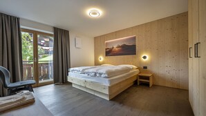 A bedroom with a bed, a desk, a chair, a wooden wall, and a window with curtains. - 1015A Valdussa Panoramic Apartment (Ortisei)