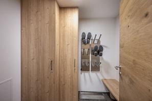 A wooden door leading to a room with a shoe rack and a bench.