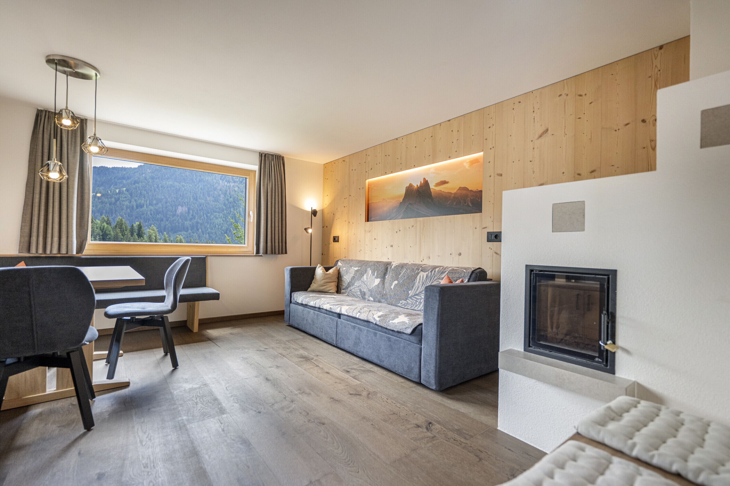 Ein modernes Wohnzimmer mit einer Couch, einem Esstisch mit Stühlen, einem Kamin und einem großen Fenster mit Bergblick.
