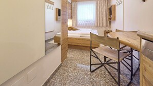 A hotel room with a bed, a desk, a chair, a mirror, and a wardrobe. - BERGLIEBE - Boutique Apartment Saalbach (Saalbach)