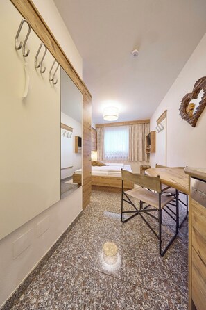 A hotel room with a bed, a desk, a chair, a mirror, and a wardrobe. - BERGLIEBE - Boutique Apartment Saalbach (Saalbach)