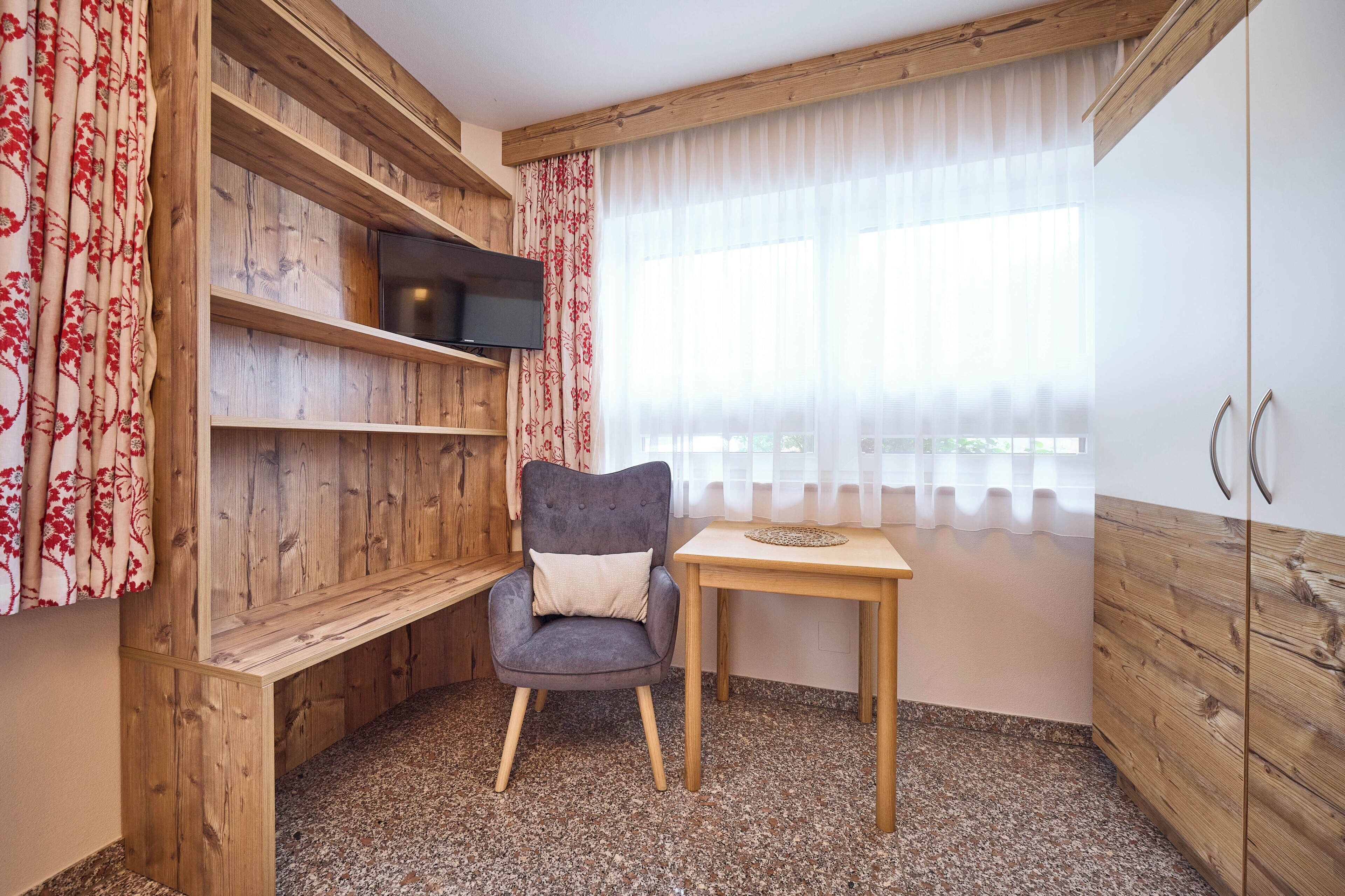 Une pièce d’angle avec un mur en bois, une chaise, une petite table et un téléviseur fixé au mur.