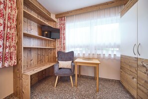 A corner room with a wooden wall, a chair, a small table, and a TV mounted on the wall.