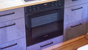 A kitchen with a built-in oven, a microwave, and a flat-screen TV mounted on the wall. - BERGLIEBE - Boutique Apartment Saalbach (Saalbach)