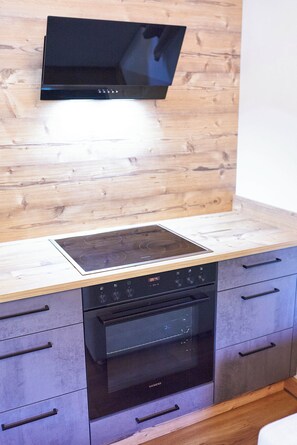 A kitchen with a built-in oven, a microwave, and a flat-screen TV mounted on the wall. - BERGLIEBE - Boutique Apartment Saalbach (Saalbach)
