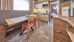 A compact kitchen with a dining area, wooden furniture, and a built-in microwave. - BERGLIEBE - Boutique Apartment Saalbach (Saalbach)