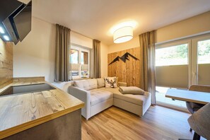 A modern living room with a sofa, a wooden accent wall, a flat-screen TV, and a dining area. - BERGLIEBE - Boutique Apartment Saalbach (Saalbach)