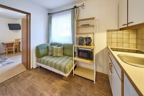 A compact living space with a sofa, a microwave, and a small kitchen area. - BERGLIEBE - Boutique Apartment Saalbach (Saalbach)