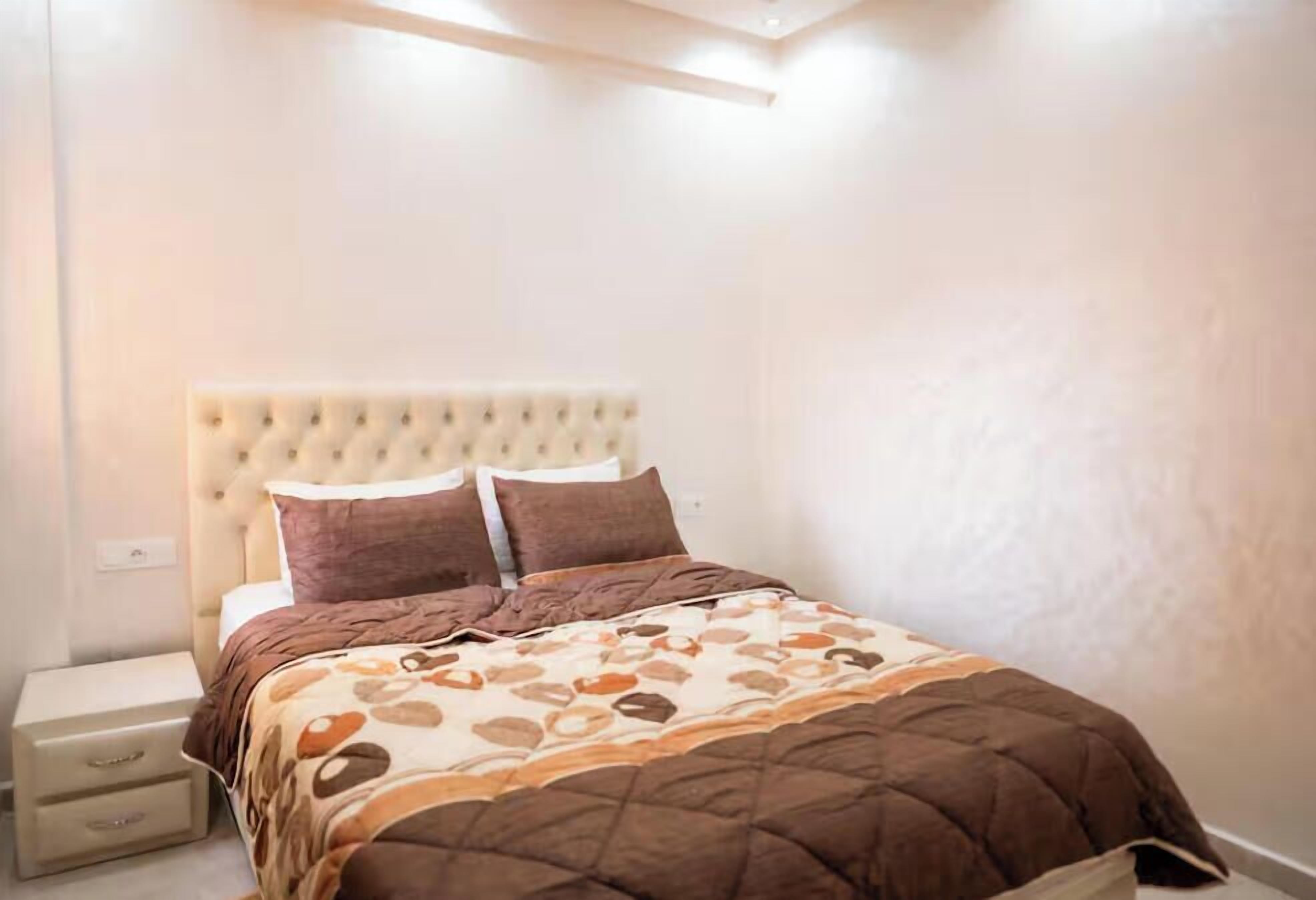 A bedroom with a tufted headboard, a bed with a patterned bedspread, and a bedside table with drawers.