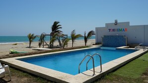 Una piscina con agua cristalina, una playa con palmeras y un edificio con el nombre 'TOIREMAR'.