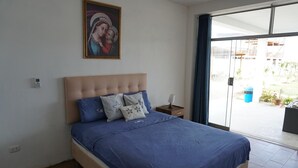 Un dormitorio con una cama, una mesita de noche, una lámpara, un cuadro en la pared y vistas al exterior.
