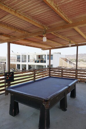 An outdoor pool table under a wooden pergola with a view of a modern building in the background.