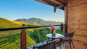 Un balcón con mesa y sillas, con vistas a campos escalonados y montañas.