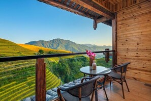 Un balcón con mesa y sillas, con vistas a campos escalonados y montañas.