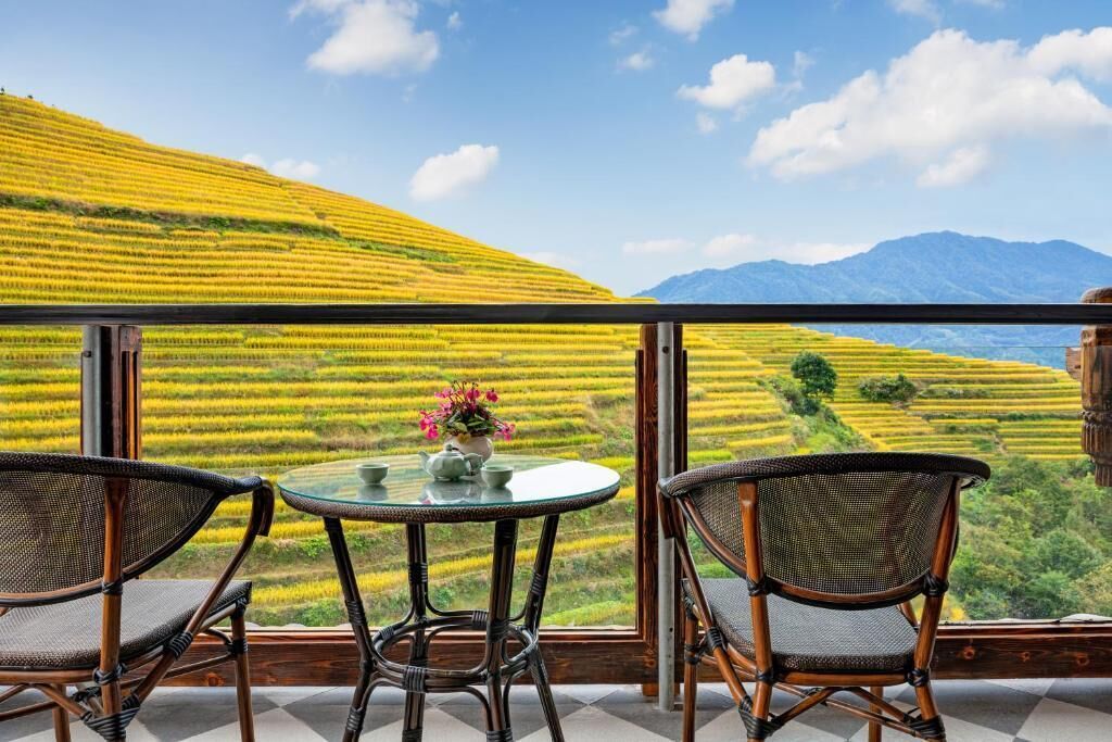 A terrace with wicker chairs and a table, overlooking terraced fields and mountains.