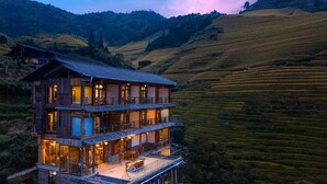 A multi-story building with terraces, set in a hilly landscape.
