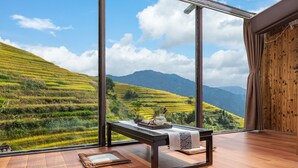 A room with a large window overlooking terraced fields and mountains.
