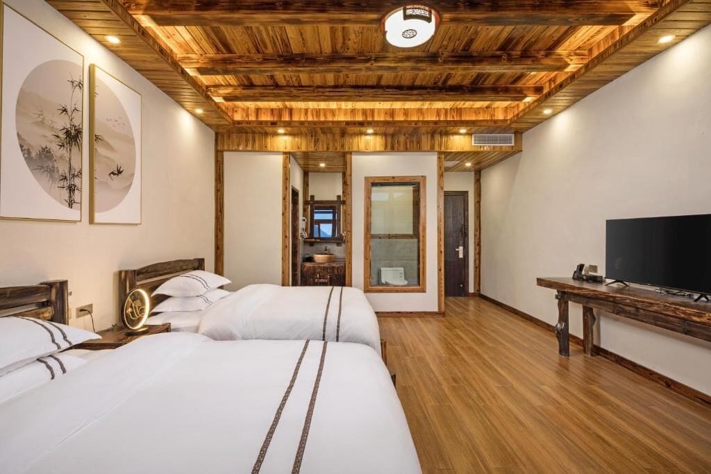 A hotel room with wooden ceiling, two beds, a TV, and artwork on the wall.