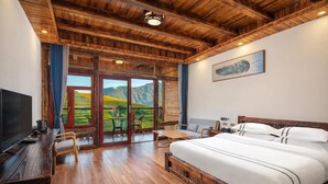 A bedroom with a wooden ceiling, a large bed, a TV, and a dining area with a view of the countryside.