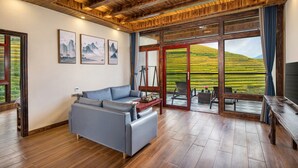 A modern living room with a wooden ceiling, a grey sofa, and a large window overlooking a green landscape.