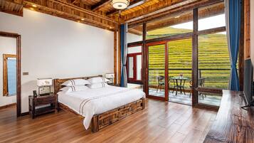 Un dormitorio con una cama de madera, una mesita de noche, un televisor y un amplio ventanal con vistas a un campo.