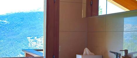 A bathroom with a wooden ceiling, a large window, and a sink with a soap dispenser.