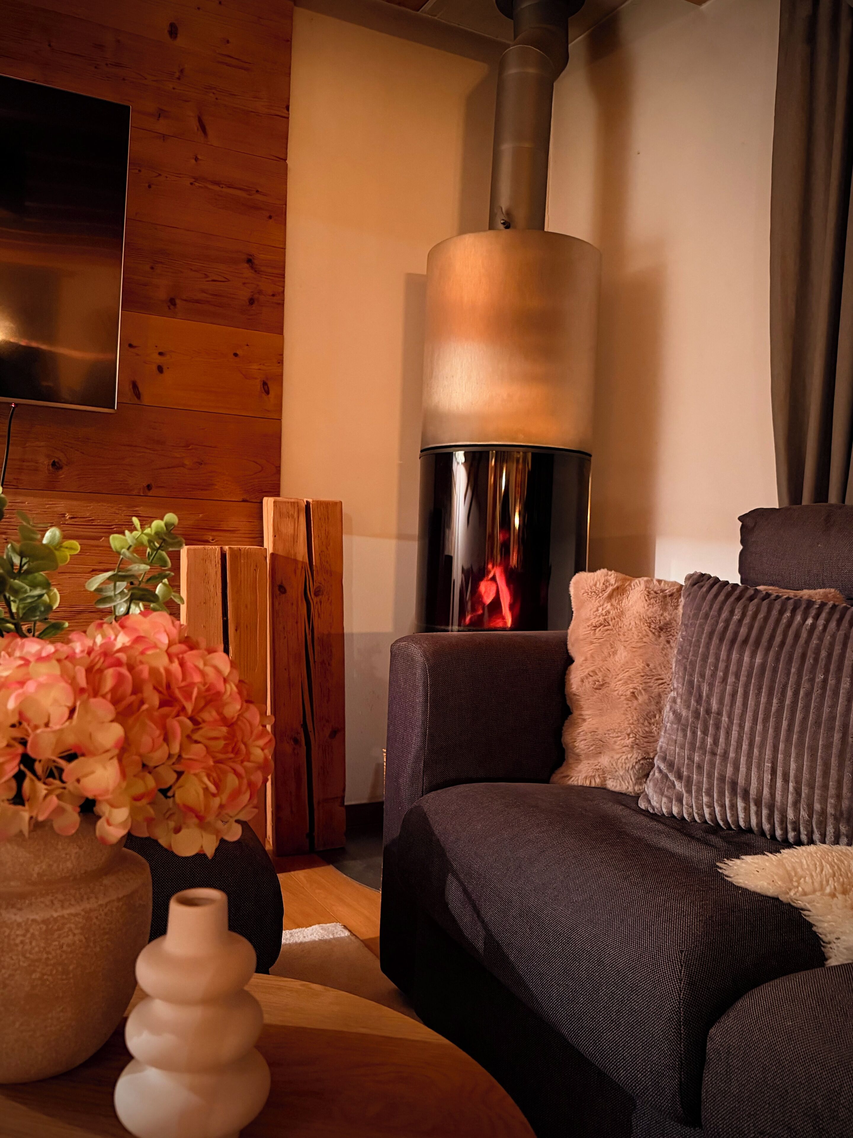 A cozy living room with a modern sofa, a fireplace, a wooden wall, and a flat-screen TV.