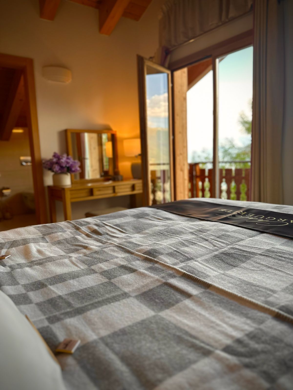 Une chambre avec une couvre-lit à carreaux, une table de chevet avec une lampe et une vue sur l’extérieur grâce à une porte coulissante.