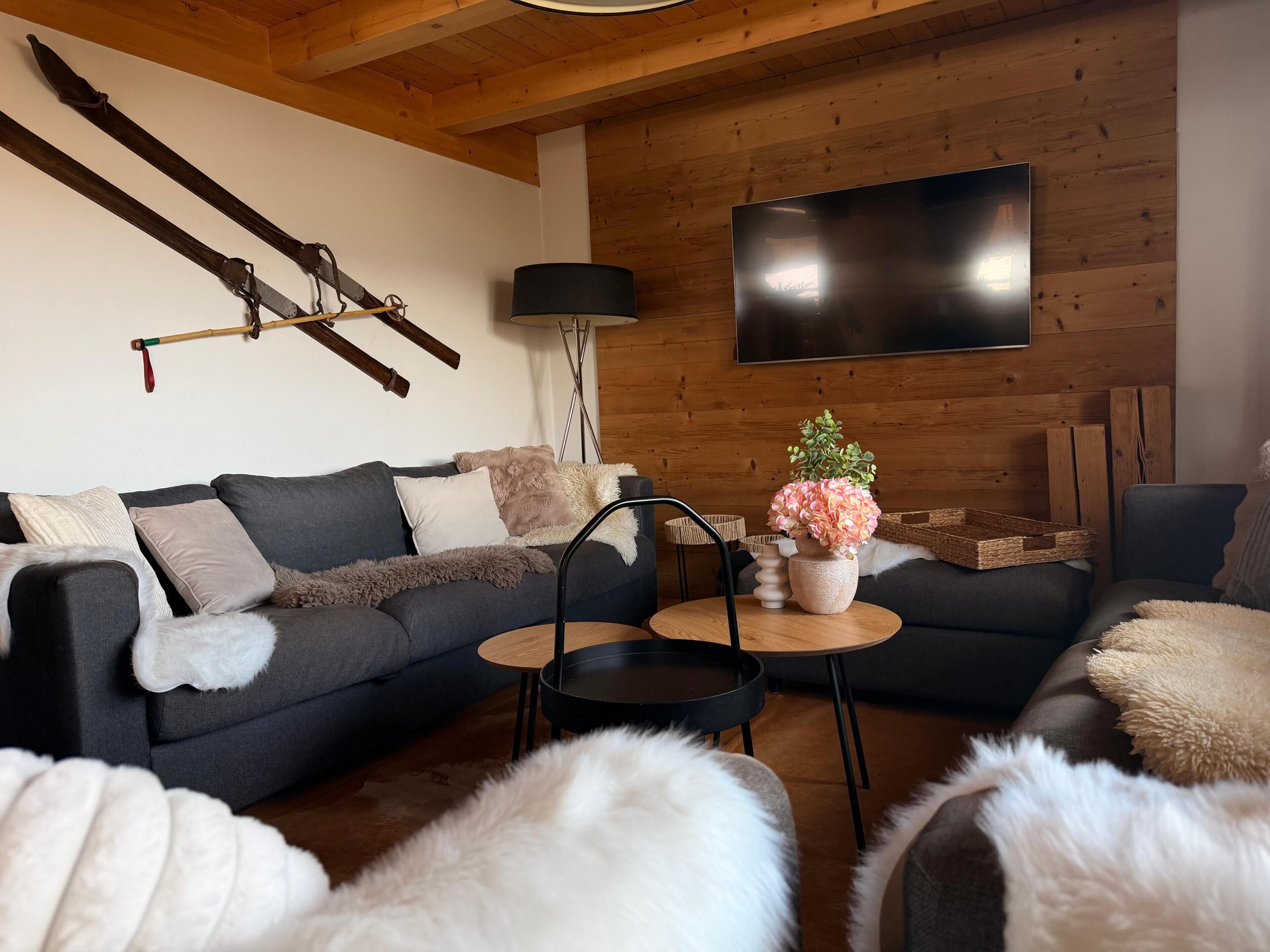 Ein modernes Wohnzimmer mit grauem Sofa, einem Couchtisch und einem an einer Holzwand montierten Fernseher.